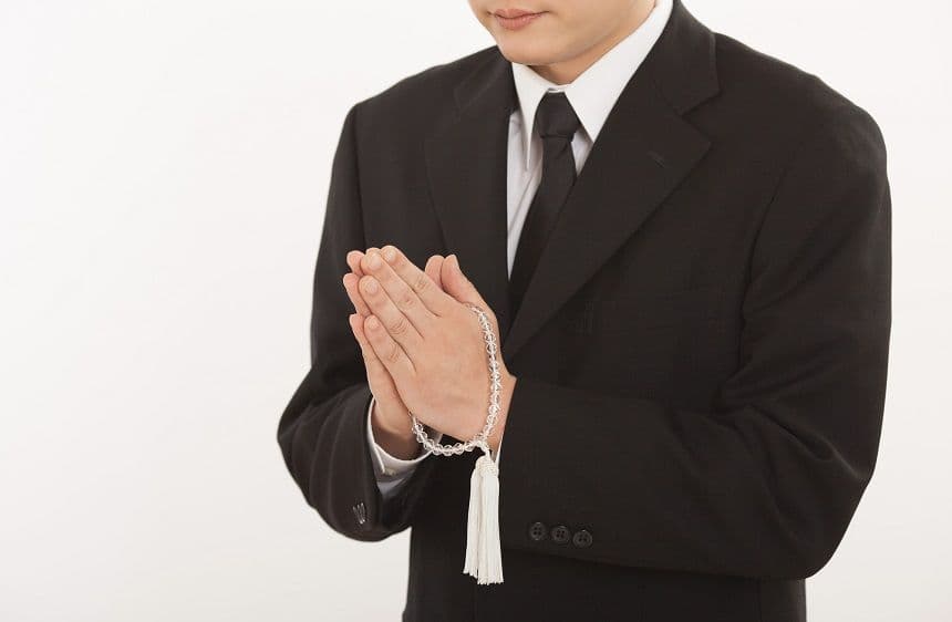 数珠を持って拝んでいる喪服姿の男性